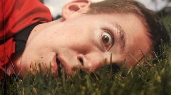 Shane Burcaw, the author of Not So Different, lies sideways in deep grass. His facial expression is one of surprise